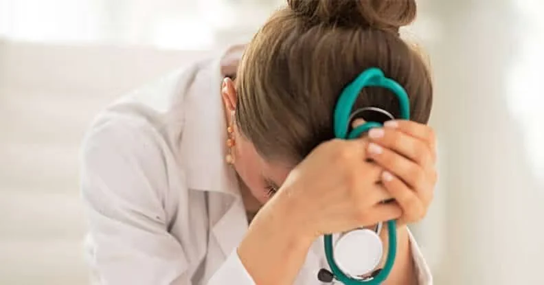 Distressed doctor with a stethoscope, head in her hands