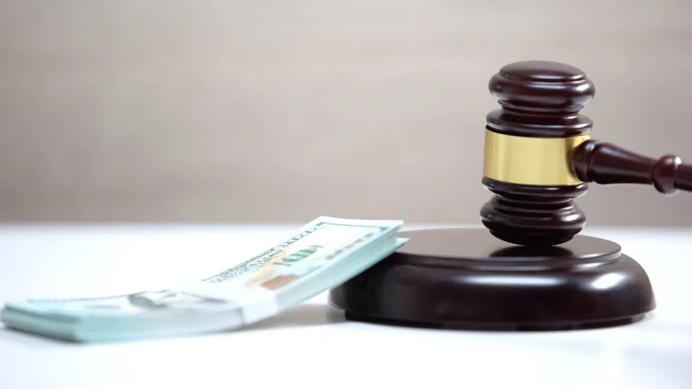Judge's gavel on a sound block beside a stack of dollar bills