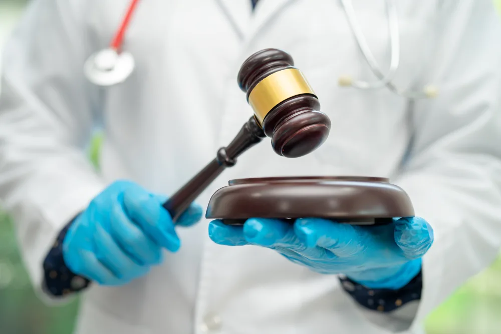 Doctor in a white coat and blue gloves holding a judge's gavel and sound block