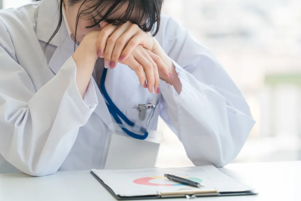 Exhausted doctor resting her head on her hands over a clipboard with a chart