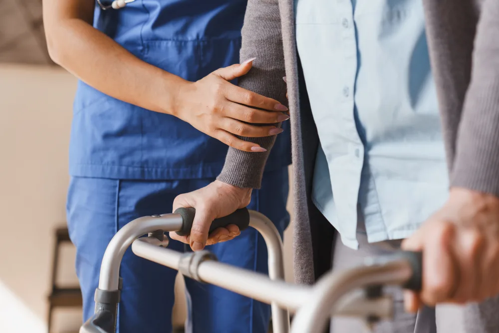 Nurse in blue scrubs steadying an elderly patient using a walker